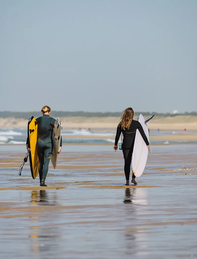Deux surfeurs portant leurs planches sur la plage de la Terrière, spot de surf proche d'un Camping Club MS..