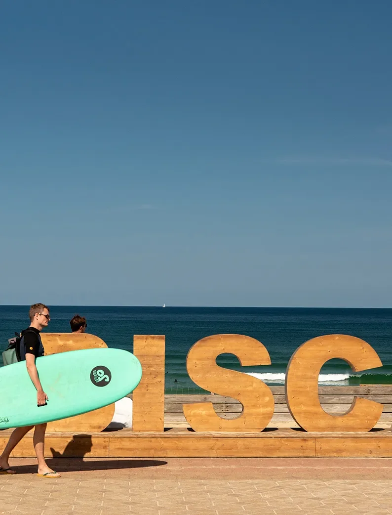 Surfeur portant sa planche devant la plage de Biscarrosse.
