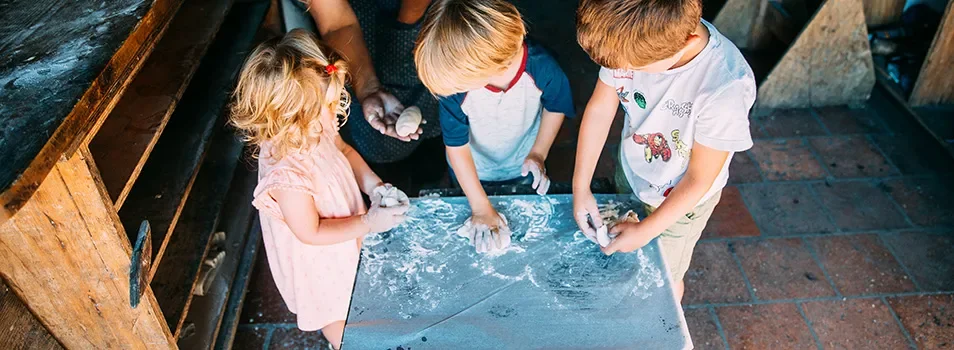 Enfants façonnant de petites boules de pâte sur une table farinée, accompagnés d’une adulte à l'Écomusée de Marquèze, à Sabres, dans les Landes.