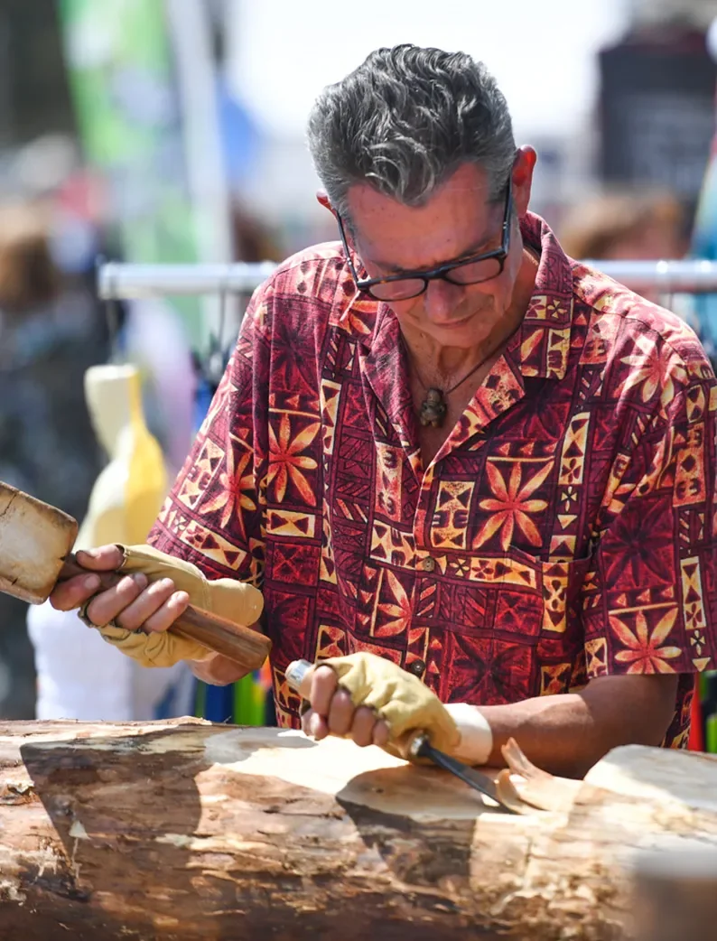Artisan polynésien sculptant du bois à l'aide d'outils traditionnels lors de la Vendée Va'a.