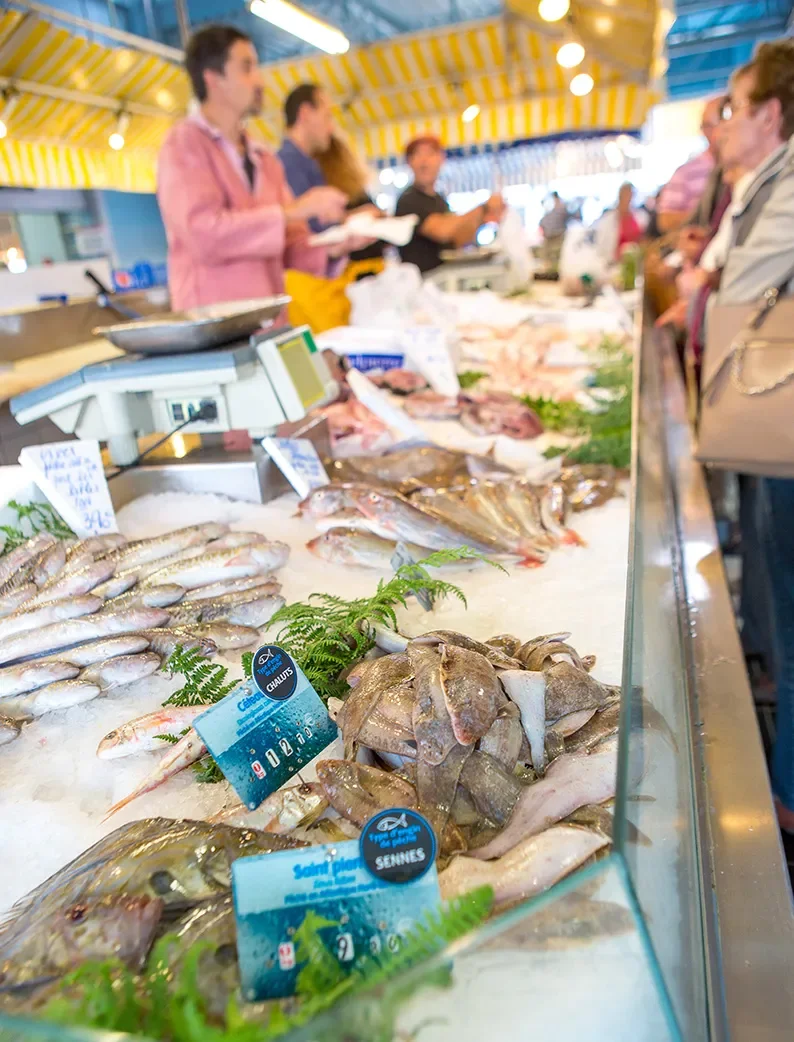 Étal de poissons frais sur glace sur un marché aux alentours de Longeville-sur-Mer avec commerçants et clients en arrière-plan.