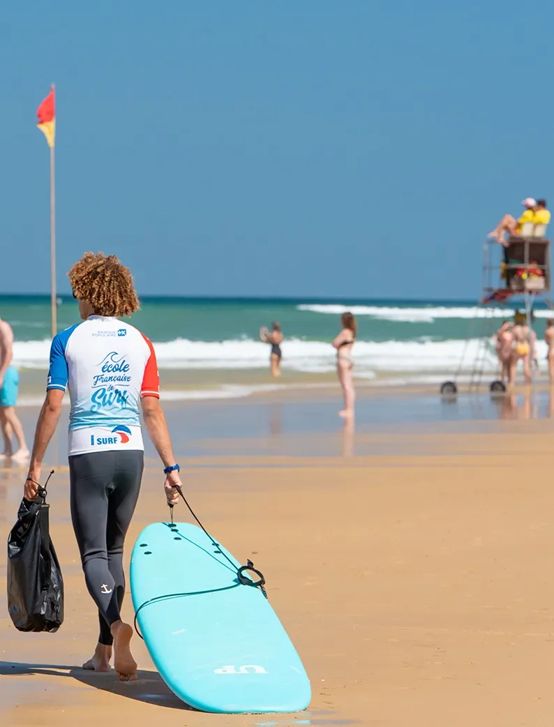 Moniteur de surf portant une planche sur la plage de Biscarrosse.