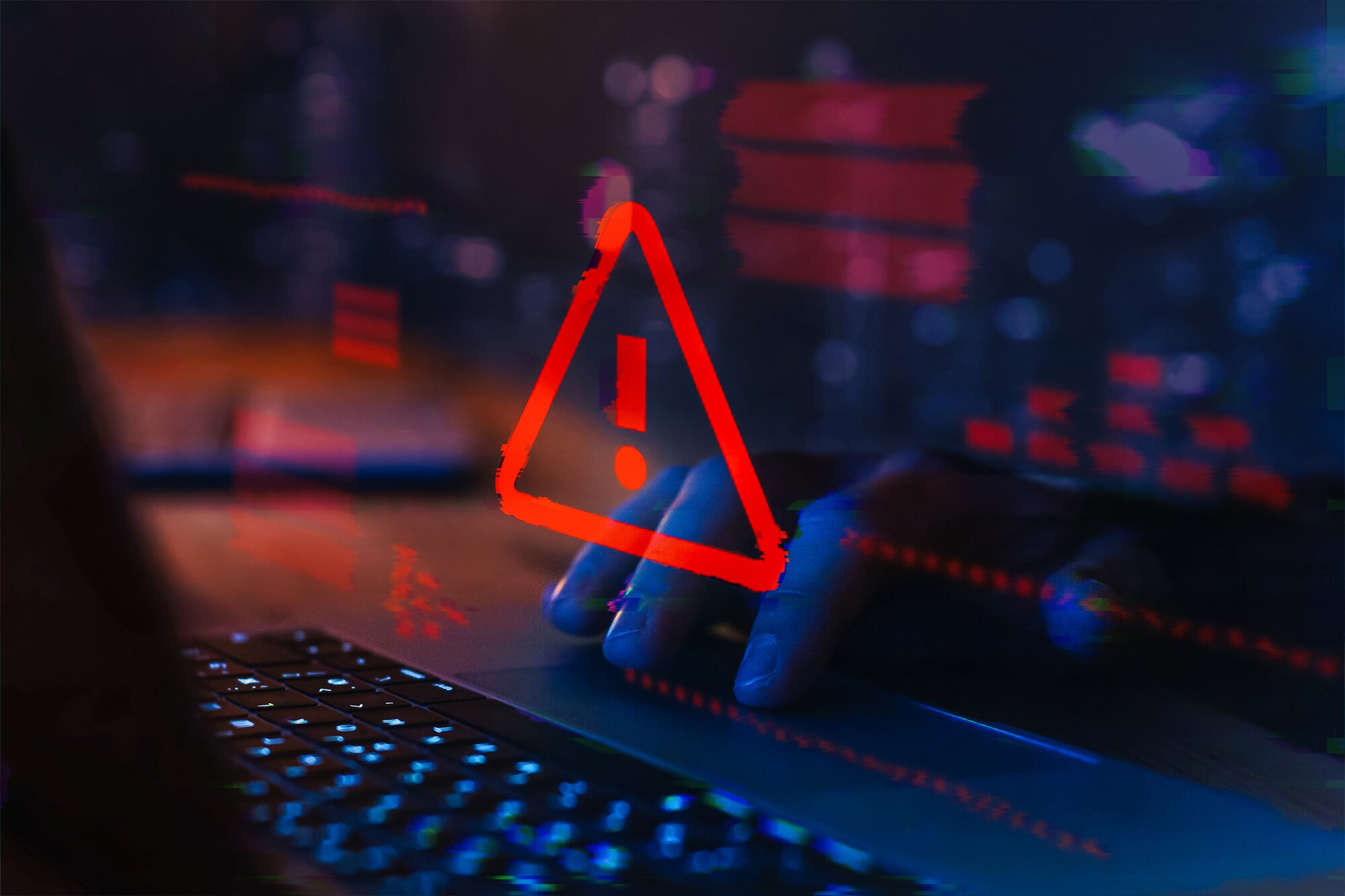 Red caution sign overlaid on a picture of a laptop with a hand on the trackpad