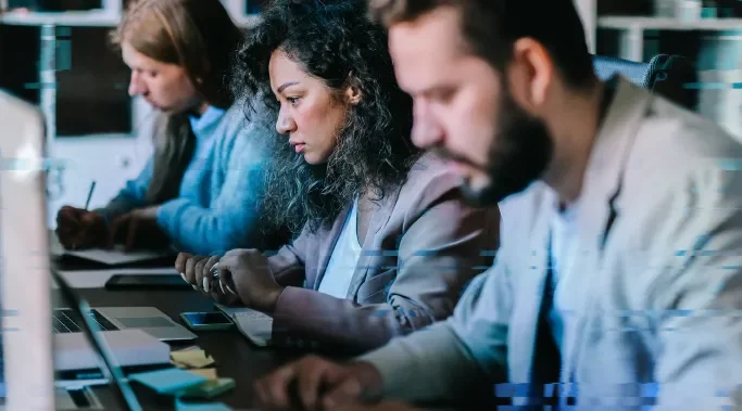 Three people sitting at a desk facing their laptops