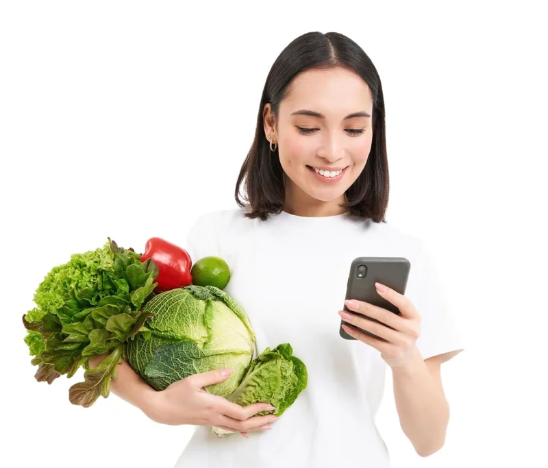 Woman holding fresh vegetables while using smartphone for effortless food tracking with AiCalorie