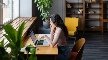Woman focused on laptop, sitting in a cozy room with plants
