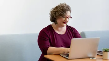 Woman in burgundy top smiling at laptop