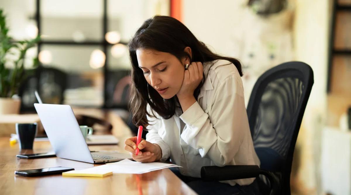 Woman focused on paperwork with a laptop nearby