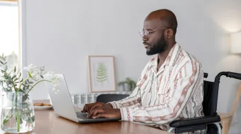 Individual in a wheelchair using a laptop at a table