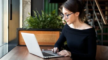 Woman in black top working on a laptop by a window