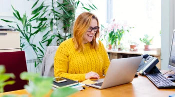 Woman in bright room, smiling at laptop