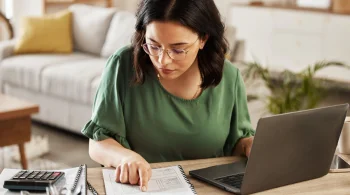 Woman focusing on paperwork with a laptop nearby