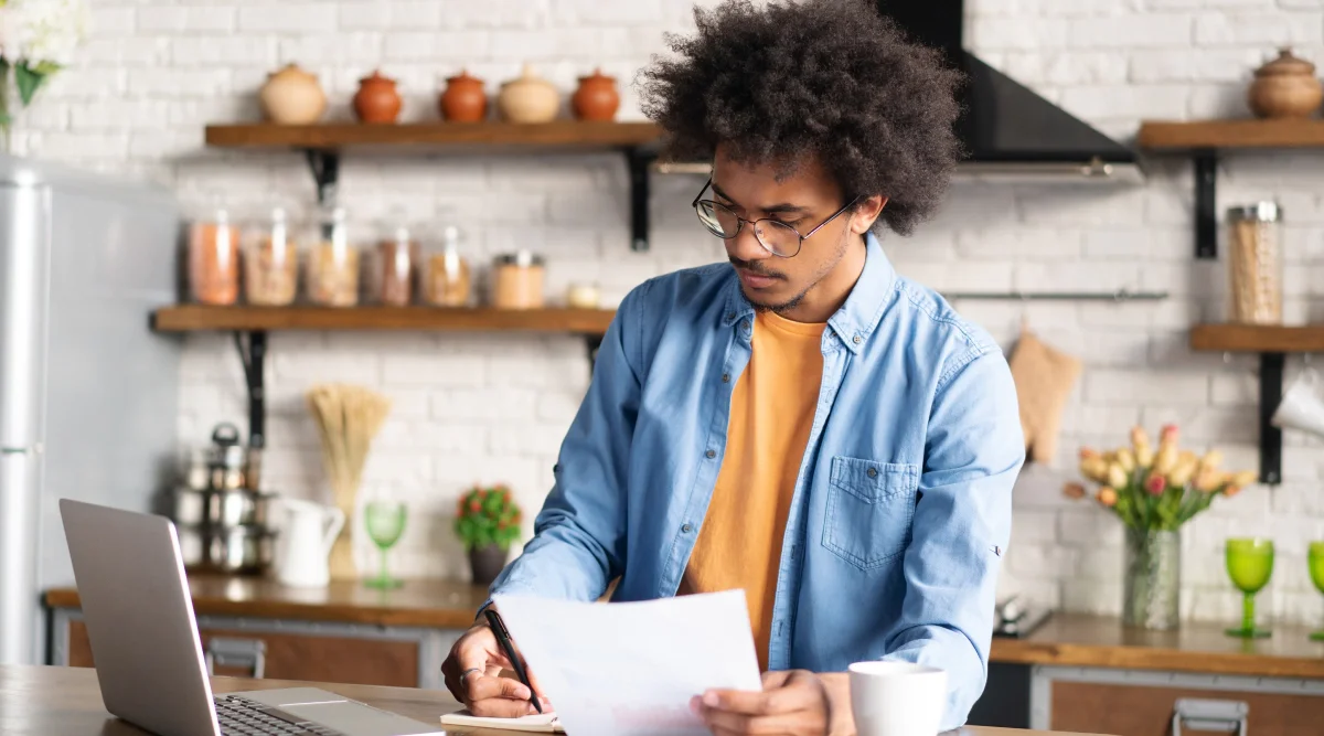 Man reviewing papers with laptop in kitchen