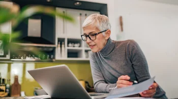 Woman reviewing papers in a kitchen with a laptop