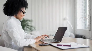 Woman in white shirt working on laptop at desk