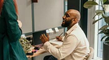 Man smiling and talking to a colleague at a desk