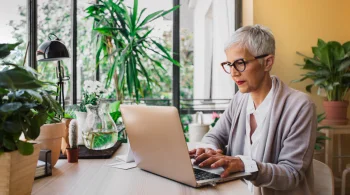 Woman reading about probate lawyer fees on laptop at a plant-filled desk.