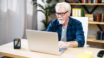 Older man in glasses working on laptop at desk