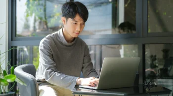 A man uses a laptop at a table outside a cafe.
