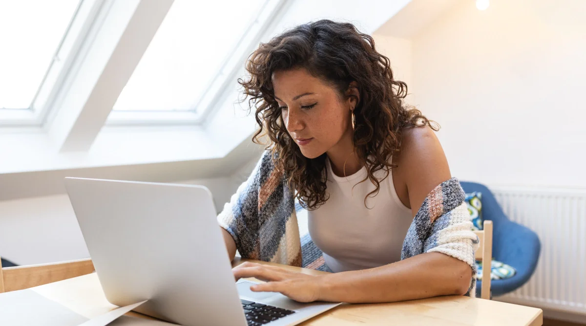 Modern young woman in casual attire at her home workstation, working on her laptop and reading about how to get a Georgia business license.