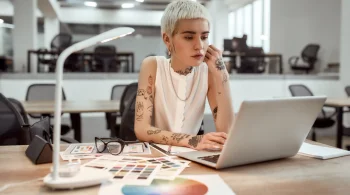 Tattooed designer working on a laptop with color charts