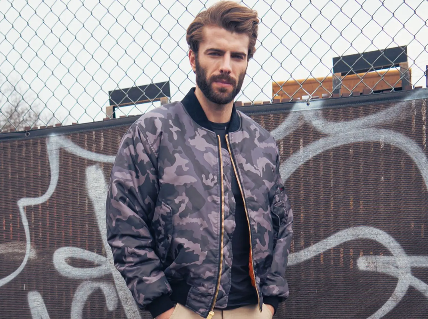 Man in black camo jacket by city fence