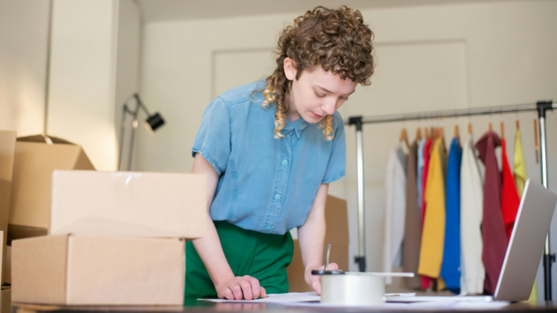 A woman standing in front of a table with delivery boxes on top, making notes.