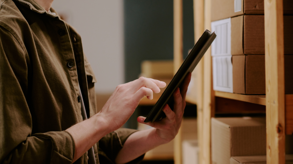 A person holding a tablet surrounded by shipping boxes.