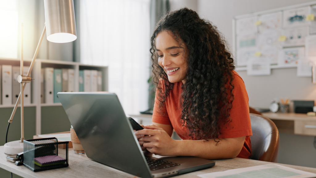 A woman with curly hair sits at a desk, engaged in her work on a laptop, showcasing concentration and productivity.