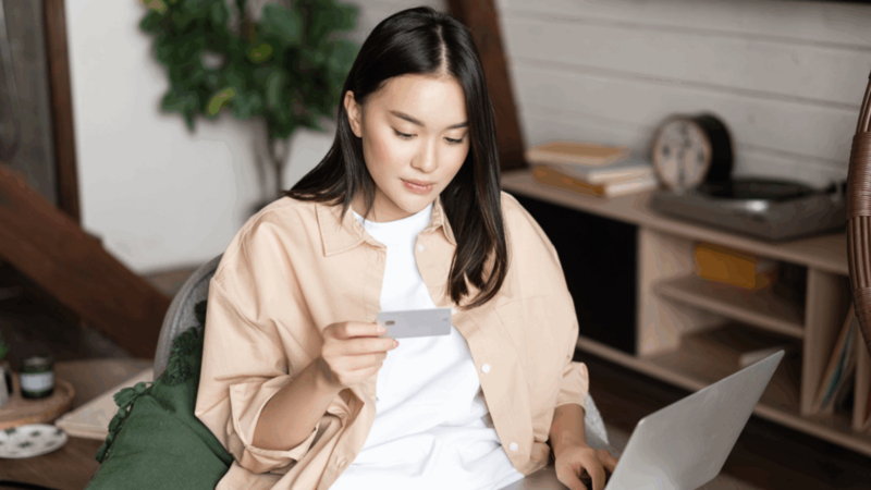 A young woman is holding a credit card and using a laptop to make an online donation to a nonprofit organization.