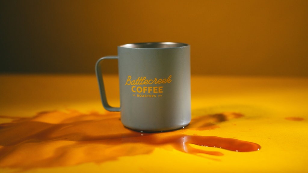 A coffee mug is placed on a table, featuring a splash of orange liquid around it.