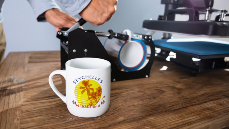 A person is using a printer next to a mug with "Seychelles Makani Island" printed on it.