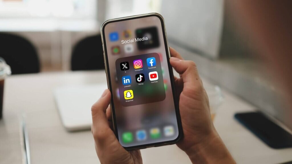 A close up shot of a mobile phone in hands with various social media apps on the screen.