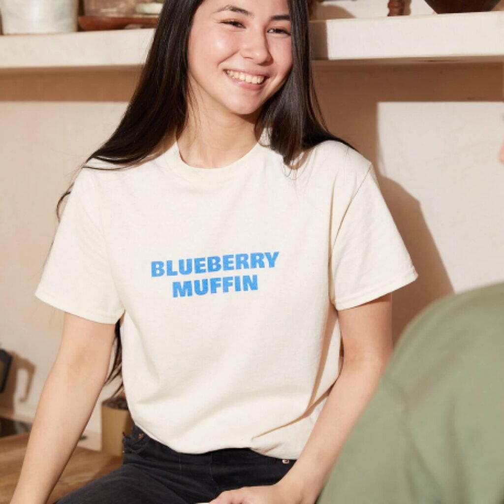 A woman wearing a cream-colored custom t-shirt with a text print on the front.