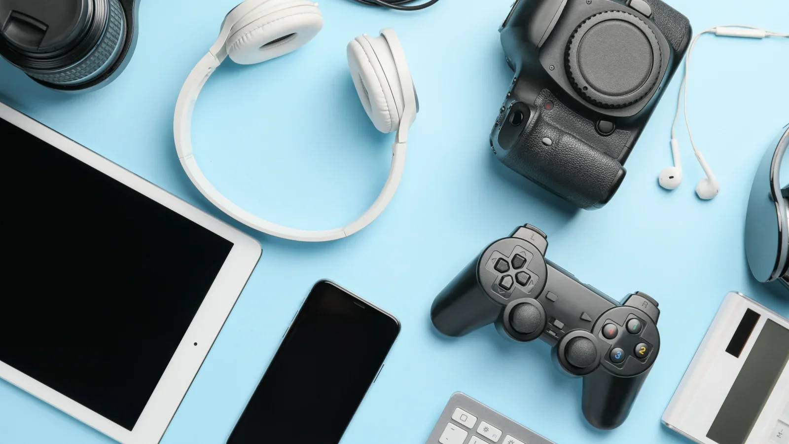 Various electronics (tablet, laptop, DSLR camera, headphones) on a blue background.
