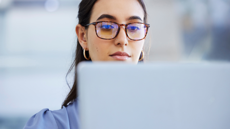 A woman wearing glasses working on a laptop, searching for Stan Store alternatives.