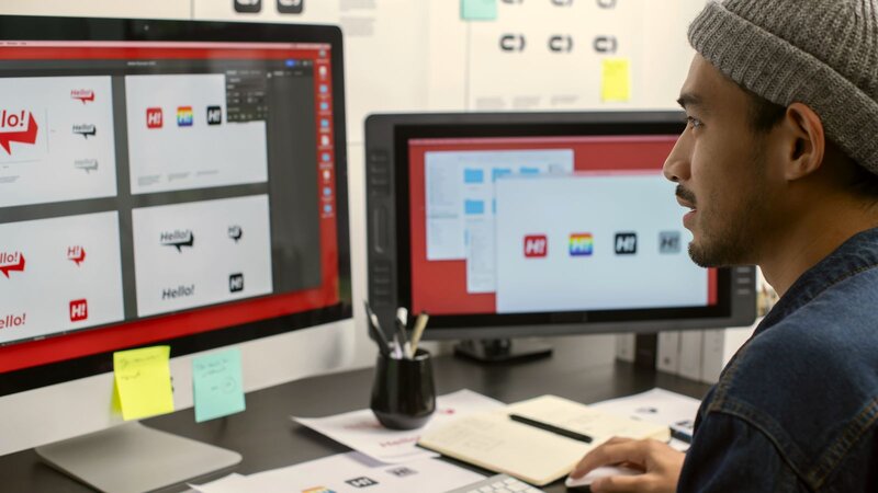 A man working at a computer, designing logos, with sticky notes on the desk.