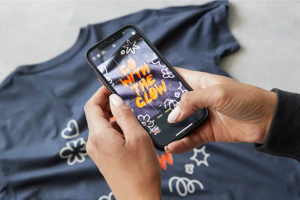 A person takes a photo of a t-shirt design that says "Go with the glow."
