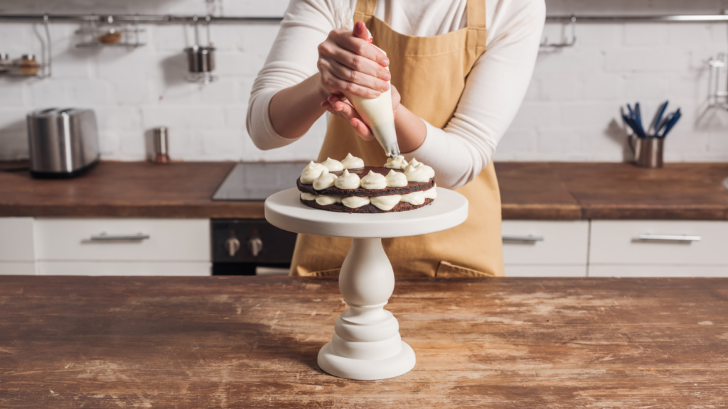 A woman decorating a chocolate cake with white frosting.