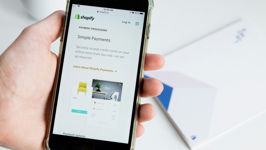 A close-up shot of a person holding a mobile phone in his hand with a Shopify page open on the screen.