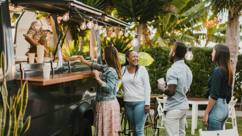 A crowd of individuals socializing and ordering food at a vibrant food truck, creating a festive atmosphere.
