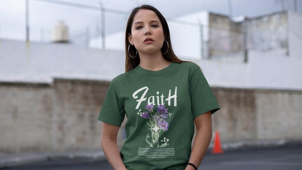 A woman wearing a custom green Fruit of the Loom 3930R t-shirt with a “Faith” text print and a flower illustration.