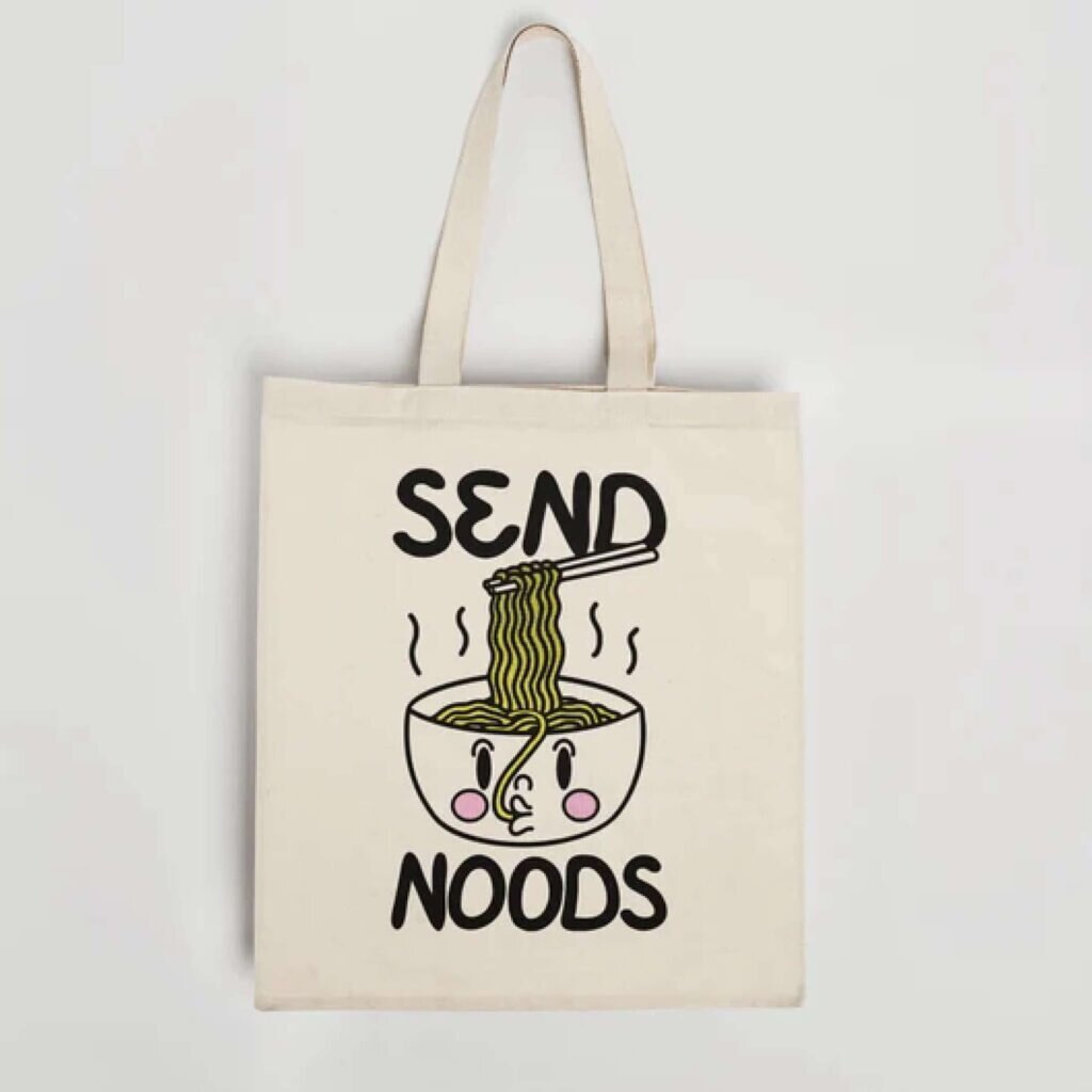 A tote bag with a smiling ramen bowl and the text “Send Noods.”