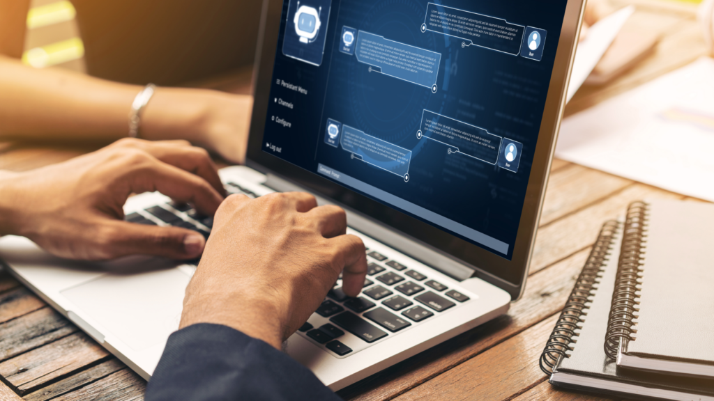 A person types on a laptop, with the screen displaying a chatbot interface, indicating an interactive conversation.
