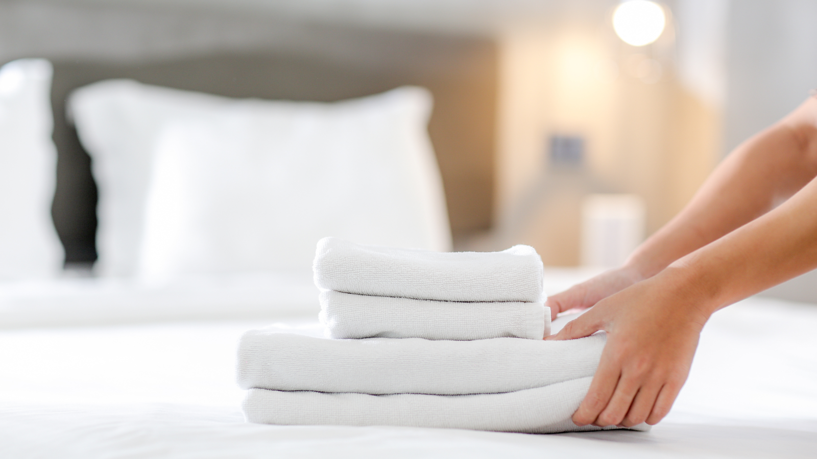 A person putting together a stack of towels on a bed.