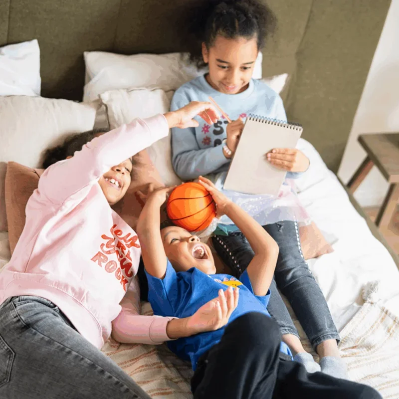 Three children (two girls, one boy) are playing on top of a bed.