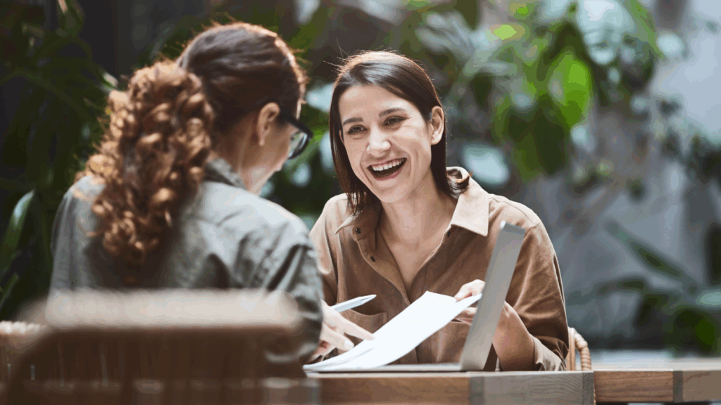 Two women seated at a table, collaborating on a laptop, engaged in discussion and sharing ideas.