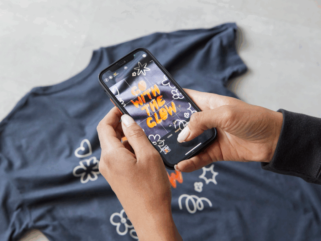 A person is taking a picture of a custom t-shirt as an example of how to make money on social media.