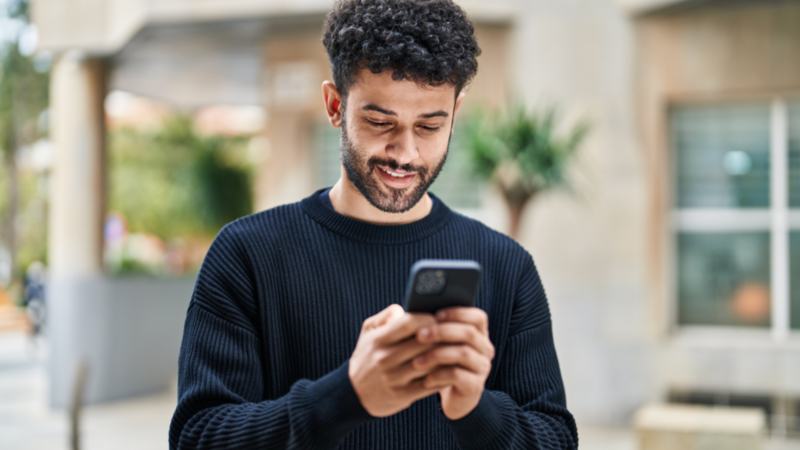 A smiling man with a beard is looking at a smartphone, learning TikTok SEO.