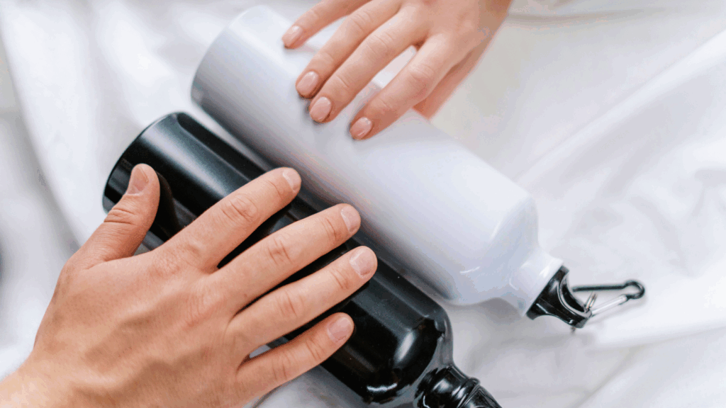 A person holds a water bottle beside another person's hand, emphasizing hydration and companionship.